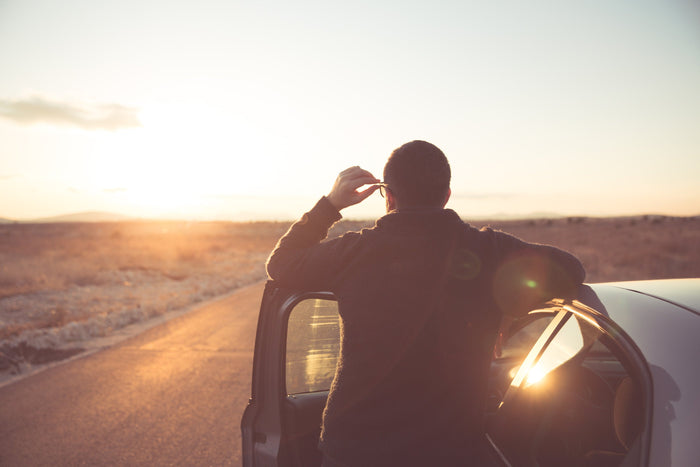 man stands outside of his car during sunset